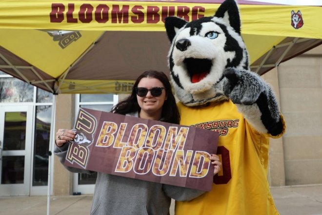 Student holds a "Bloom Bound" sign with the Husky mascot