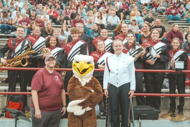 Members of the Lock Haven Marching Band pose for a photo with the Bald Eagle mascot in the stands at a football game.