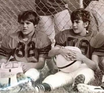 A black and white photo of two boys sitting down in football gear.