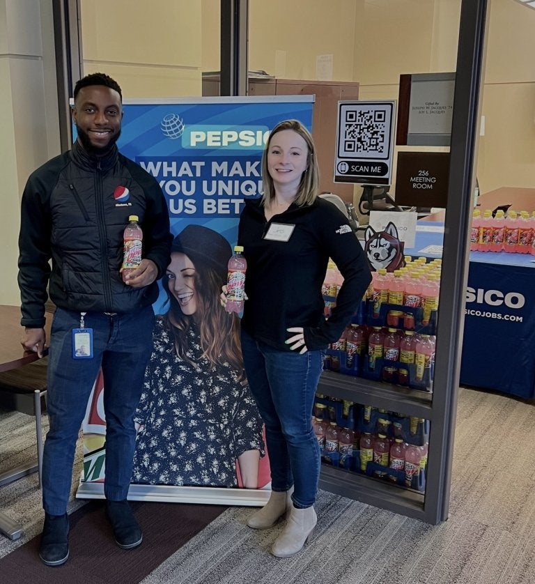 Two people standing in front of a sign. 