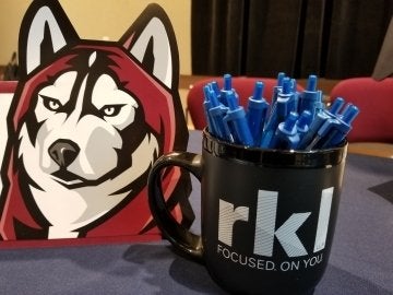 Bloomsburg Husky next to a mug filled pens. 
