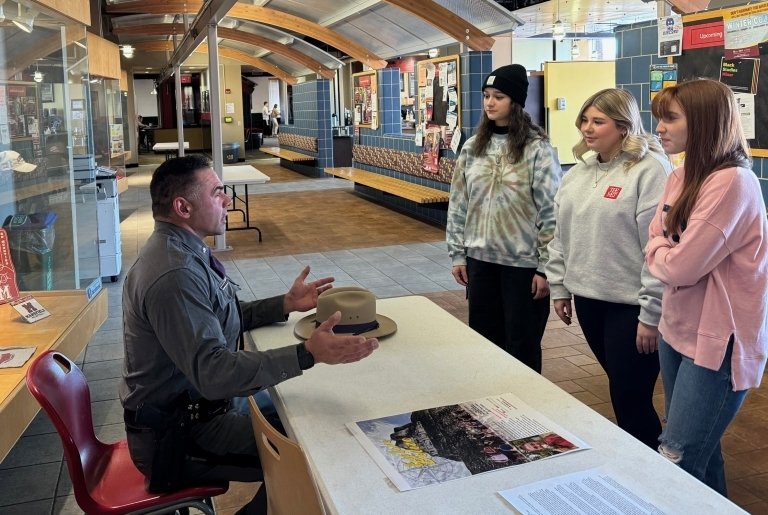 Officer sitting at a table talking with three standing students.