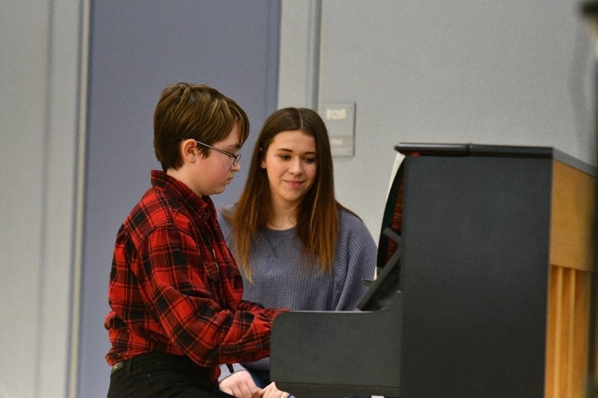 One person playing piano and one person watching. 