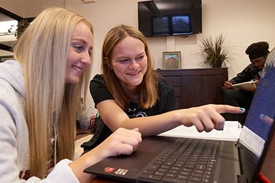 Two Commonwealth University students pointing at a laptop and smiling